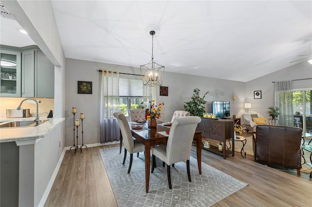 dining area featuring ceiling fan with notable chandelier, wood-type flooring, sink, and lofted ceiling