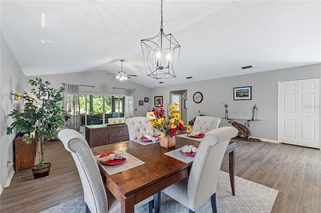 dining space with ceiling fan with notable chandelier, light hardwood / wood-style floors, and vaulted ceiling