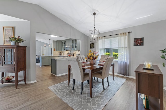 dining space with hardwood / wood-style flooring, lofted ceiling, sink, and a chandelier