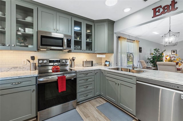 kitchen with an inviting chandelier, sink, light stone countertops, light wood-type flooring, and appliances with stainless steel finishes