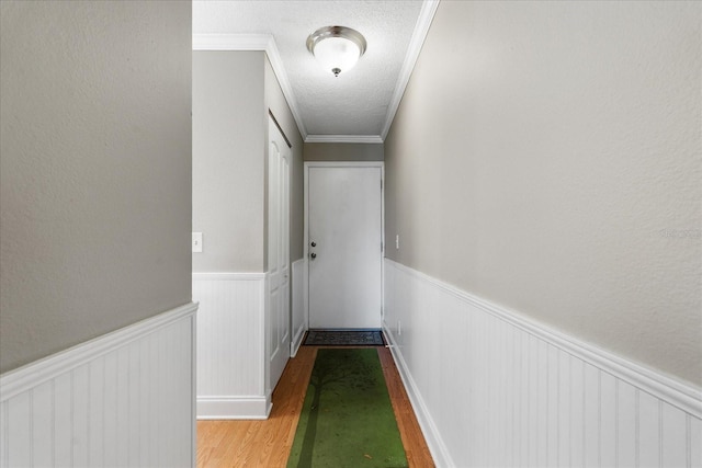 hallway featuring light wood-type flooring, a textured ceiling, and ornamental molding