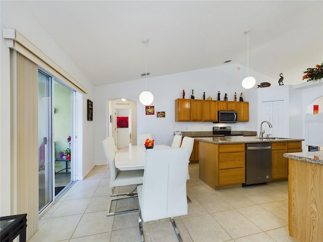 kitchen featuring vaulted ceiling, appliances with stainless steel finishes, brown cabinetry, an island with sink, and pendant lighting