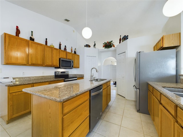 kitchen with brown cabinets, decorative light fixtures, stainless steel appliances, a sink, and an island with sink