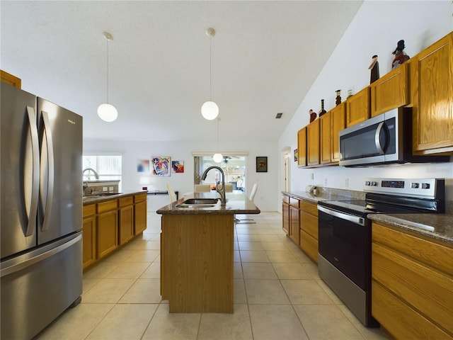 kitchen featuring decorative light fixtures, a sink, appliances with stainless steel finishes, dark countertops, and a center island with sink