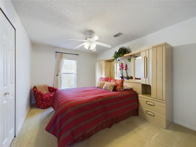 bedroom with a textured ceiling, a ceiling fan, visible vents, and light colored carpet