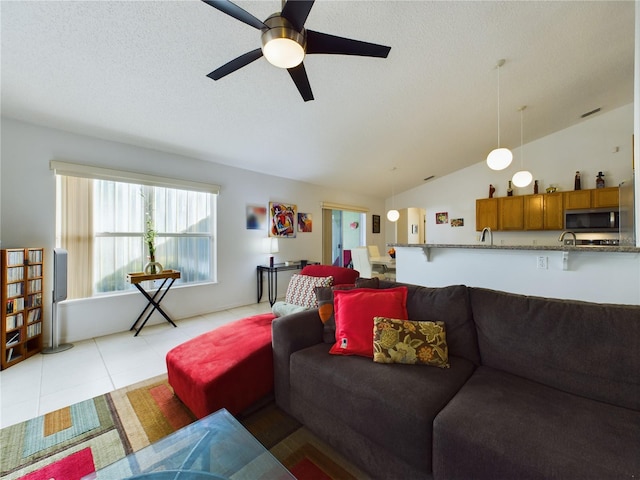 living area with lofted ceiling, ceiling fan, a textured ceiling, and light tile patterned floors