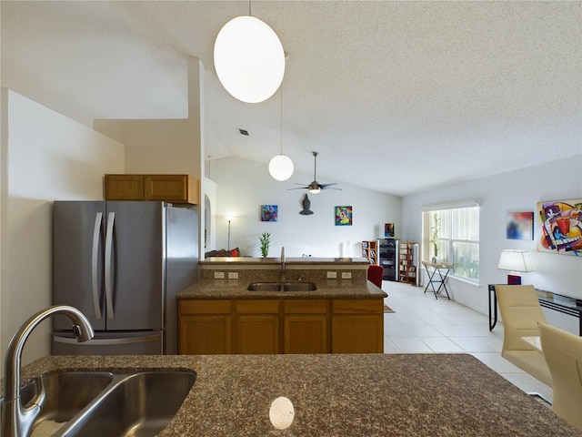 kitchen featuring freestanding refrigerator, brown cabinetry, a sink, and decorative light fixtures