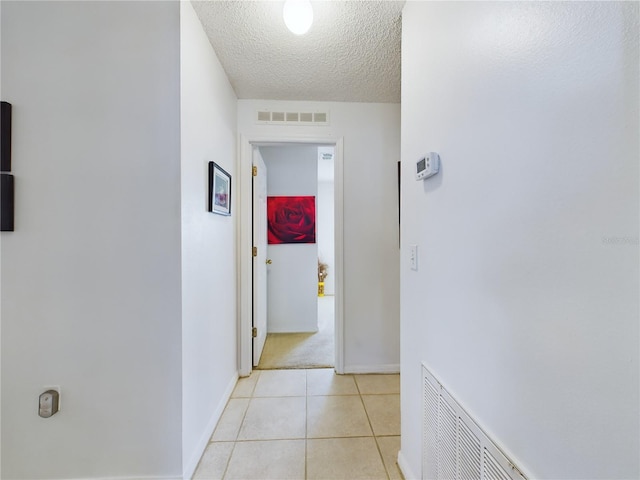 corridor featuring visible vents, a textured ceiling, baseboards, and light tile patterned flooring