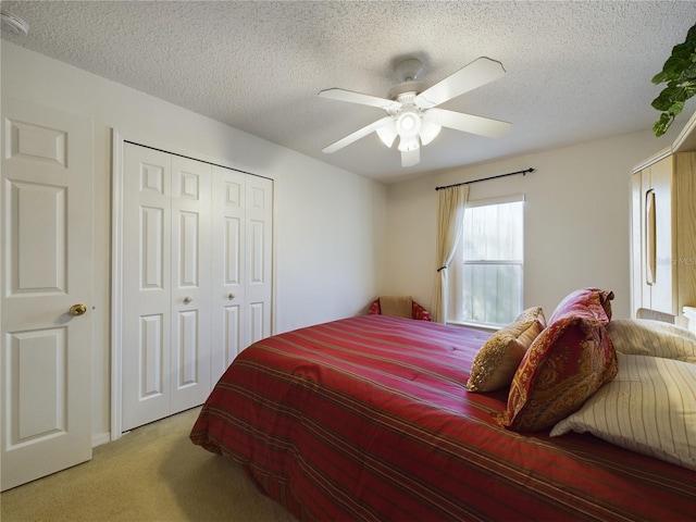 bedroom with a textured ceiling, a closet, a ceiling fan, and light colored carpet