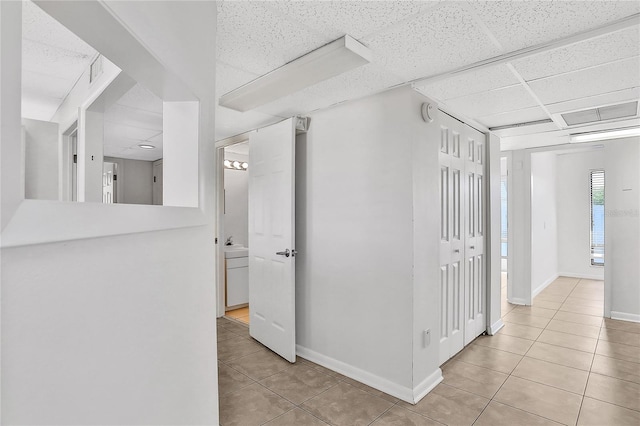 hallway featuring a drop ceiling and light tile patterned floors