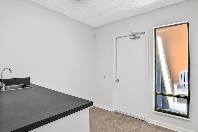 kitchen with white cabinets, a paneled ceiling, sink, and light tile patterned floors