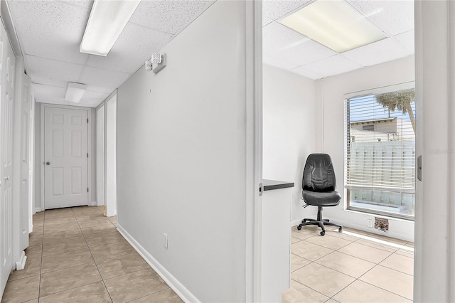 hall with a paneled ceiling and light tile patterned flooring