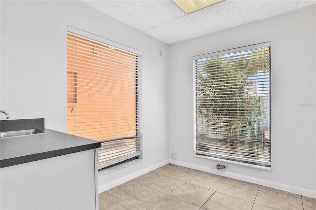 unfurnished dining area featuring light tile patterned floors, a paneled ceiling, and sink