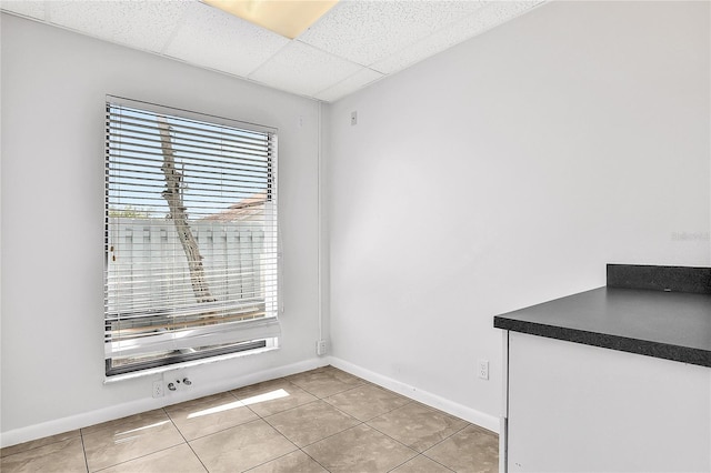 unfurnished dining area featuring light tile patterned floors, a drop ceiling, and a healthy amount of sunlight