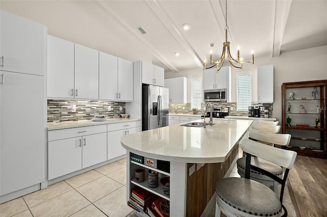 kitchen with pendant lighting, a kitchen island with sink, white cabinets, sink, and appliances with stainless steel finishes