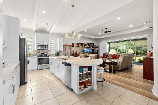 kitchen with white cabinetry, a kitchen island with sink, ceiling fan with notable chandelier, and appliances with stainless steel finishes