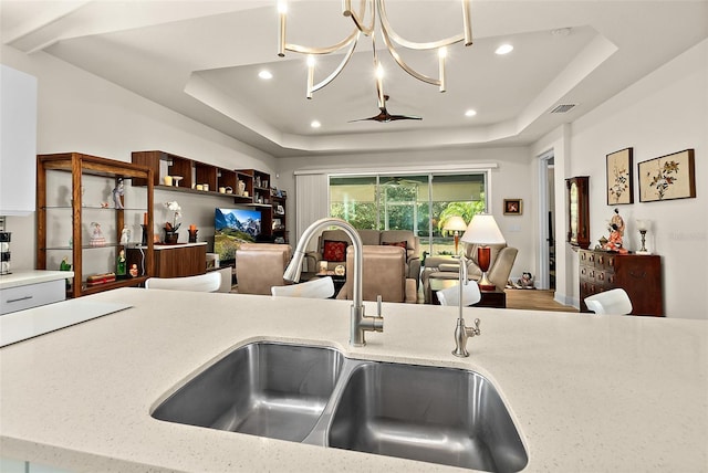 kitchen featuring light stone countertops, sink, hanging light fixtures, a chandelier, and a tray ceiling