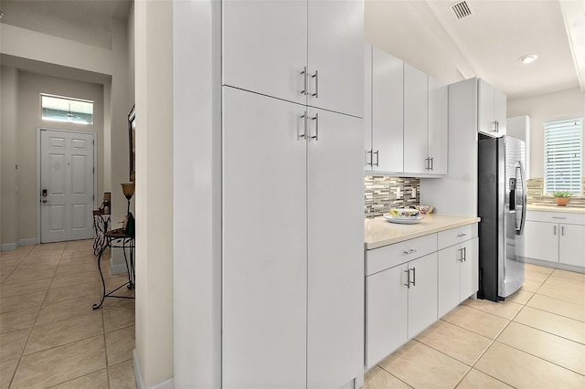 kitchen featuring white cabinets, stainless steel fridge, light tile patterned floors, and tasteful backsplash