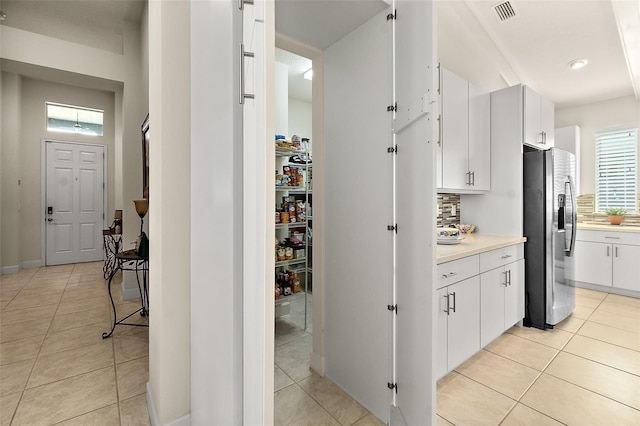 interior space featuring decorative backsplash, stainless steel fridge, light tile patterned floors, and white cabinetry