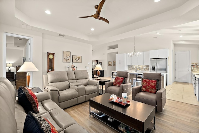 living room featuring a tray ceiling, light hardwood / wood-style floors, and ceiling fan with notable chandelier