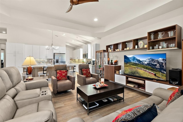 living room featuring ceiling fan with notable chandelier, light wood-type flooring, and lofted ceiling