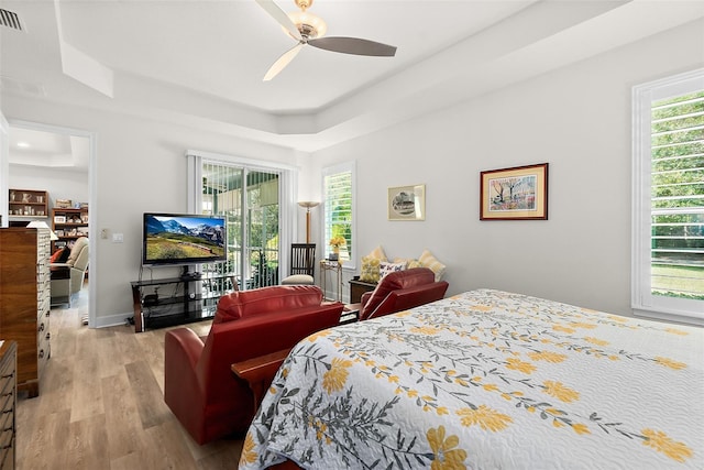 bedroom featuring a raised ceiling, access to exterior, ceiling fan, and light wood-type flooring