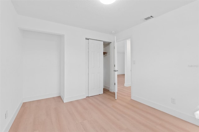 unfurnished bedroom featuring a textured ceiling, light hardwood / wood-style floors, and a closet