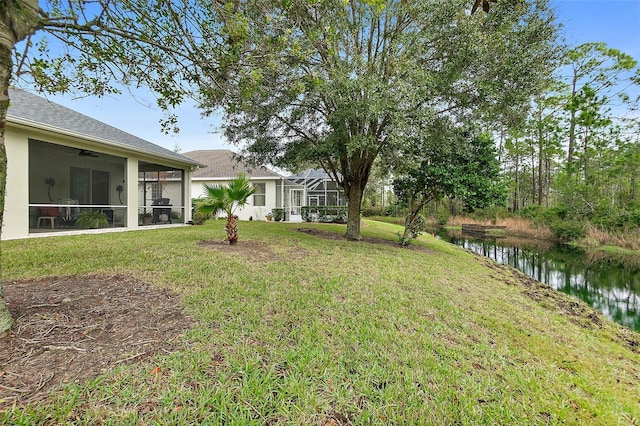 view of yard featuring a sunroom, ceiling fan, and a water view