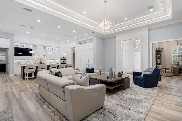 living room featuring light hardwood / wood-style flooring, a raised ceiling, crown molding, and a chandelier