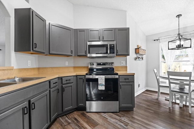 kitchen featuring pendant lighting, lofted ceiling, gray cabinets, appliances with stainless steel finishes, and a notable chandelier