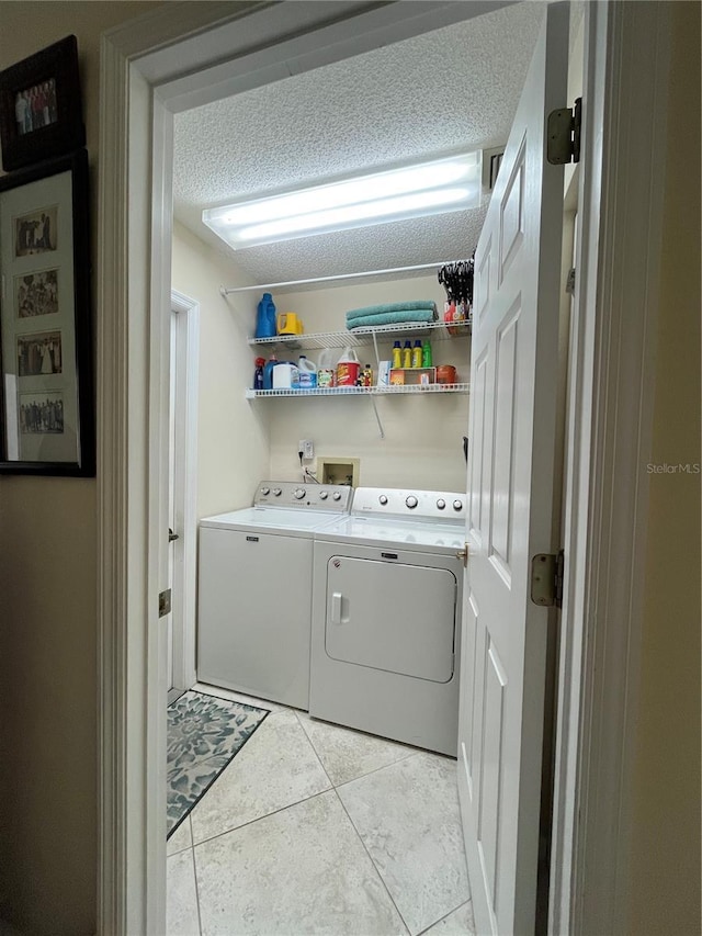 clothes washing area with separate washer and dryer, light tile patterned floors, and a textured ceiling