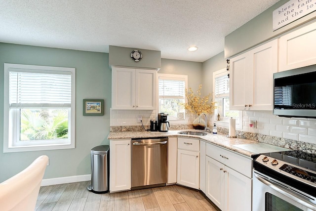 kitchen with tasteful backsplash, sink, white cabinets, light hardwood / wood-style floors, and stainless steel appliances