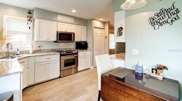 kitchen with appliances with stainless steel finishes, white cabinetry, sink, decorative backsplash, and light hardwood / wood-style floors