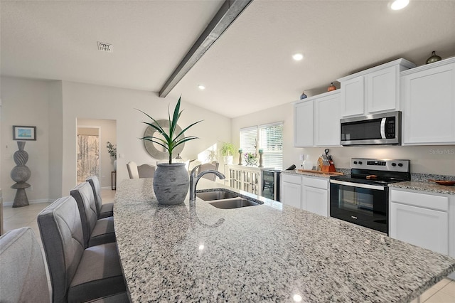 kitchen featuring a kitchen island with sink, white cabinets, sink, appliances with stainless steel finishes, and a breakfast bar area