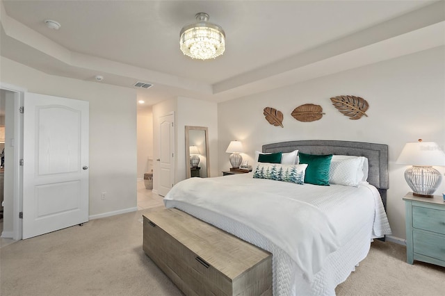 bedroom featuring light colored carpet, connected bathroom, and a tray ceiling