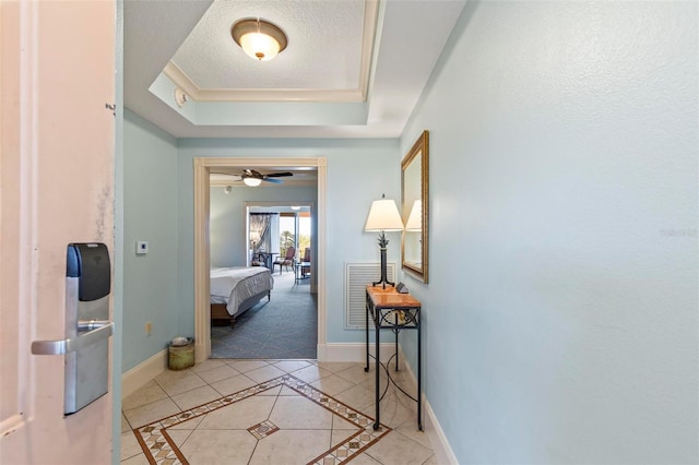 hall with light tile patterned flooring, a raised ceiling, and a textured ceiling