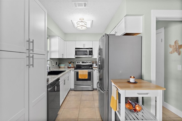 kitchen with sink, light tile patterned floors, a textured ceiling, white cabinetry, and stainless steel appliances