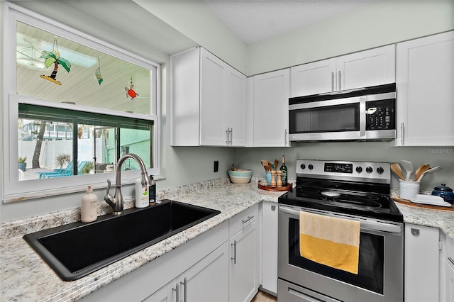 kitchen with white cabinetry, sink, light stone counters, and appliances with stainless steel finishes