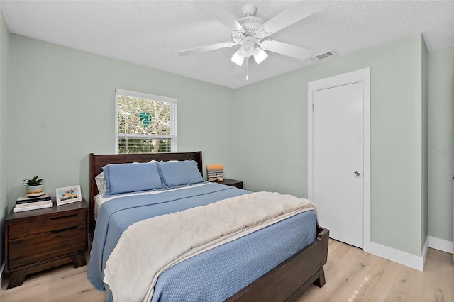 bedroom with ceiling fan, light hardwood / wood-style floors, and a textured ceiling