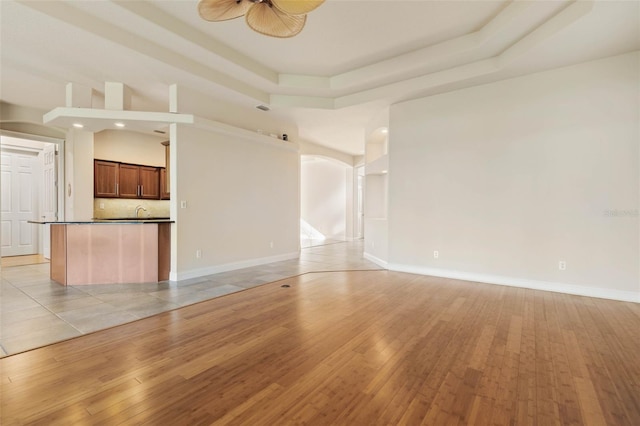 unfurnished living room with a raised ceiling, ceiling fan, and light tile patterned floors