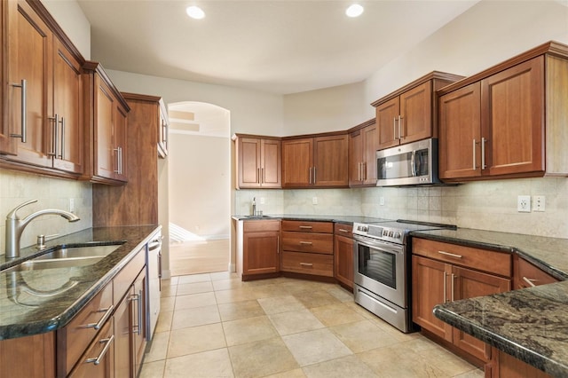 kitchen with tasteful backsplash, dark stone countertops, sink, and stainless steel appliances