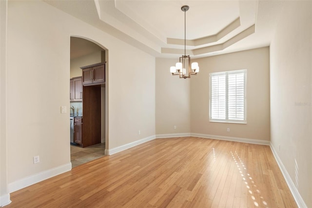 unfurnished room featuring an inviting chandelier, a tray ceiling, and light hardwood / wood-style flooring