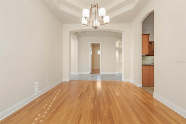 unfurnished dining area featuring light wood-type flooring, a tray ceiling, and an inviting chandelier