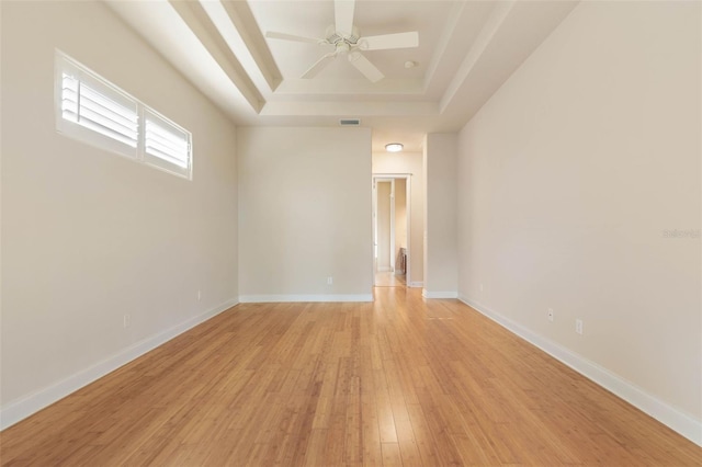 empty room featuring a tray ceiling, ceiling fan, and light hardwood / wood-style floors