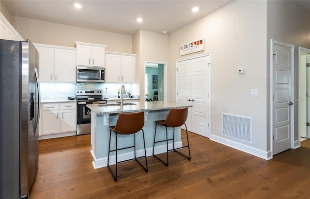 kitchen with appliances with stainless steel finishes, light stone counters, sink, white cabinetry, and an island with sink