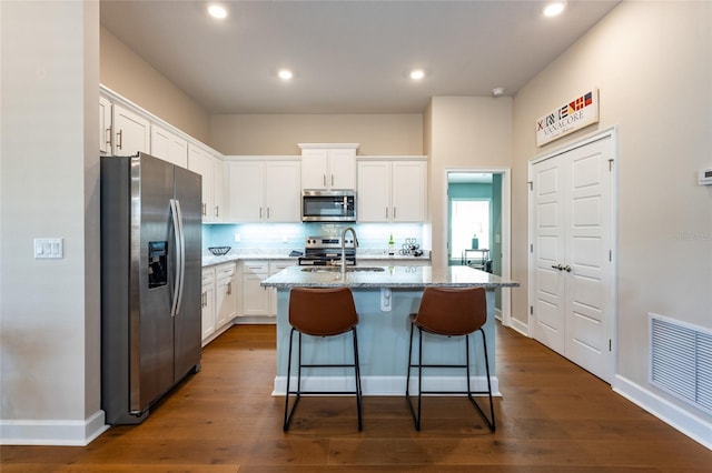 kitchen featuring white cabinetry, stainless steel appliances, light stone counters, backsplash, and an island with sink