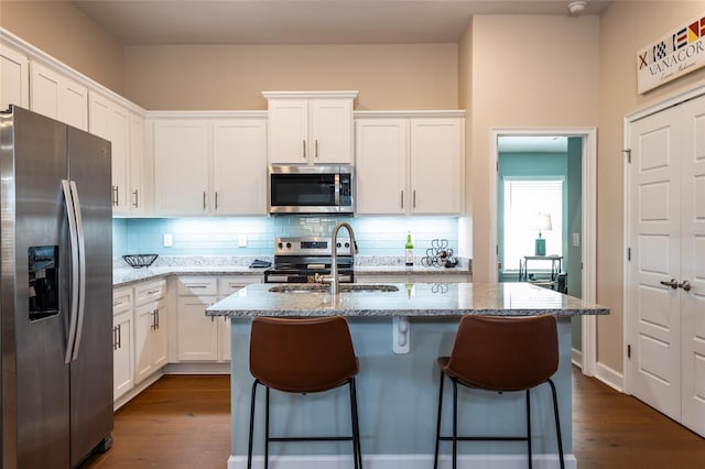 kitchen with tasteful backsplash, light stone counters, stainless steel appliances, a kitchen island with sink, and white cabinets