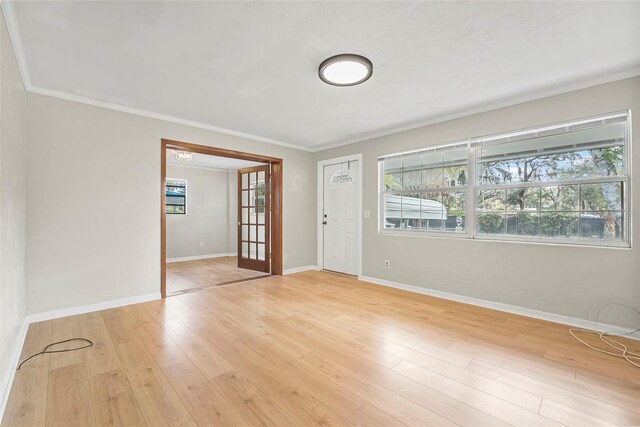 empty room featuring french doors, ornamental molding, and light wood-type flooring