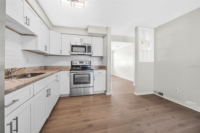 kitchen with appliances with stainless steel finishes, light wood-type flooring, tasteful backsplash, sink, and white cabinets