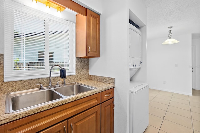 kitchen featuring a textured ceiling, sink, light tile patterned floors, stacked washer and clothes dryer, and hanging light fixtures